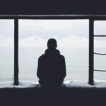 man sitting on ledge looking out at the ocean